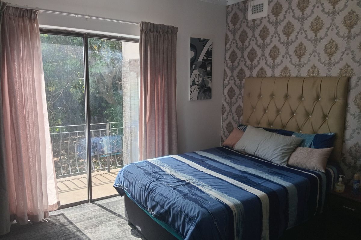 A bedroom featuring decorative wallpaper, a tufted headboard, and a sliding glass door providing access to a private balcony.