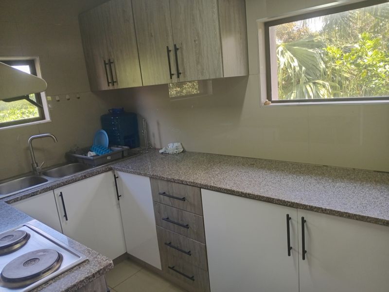 A functional kitchen featuring modern two-tone cabinetry, granite countertops, a stainless steel sink, and an integrated electric hob with ample workspace.