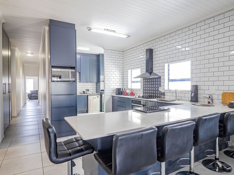 Modern kitchen featuring dark blue cabinetry, white subway tile backsplash, quartz countertops, and a breakfast bar island with integrated appliances.