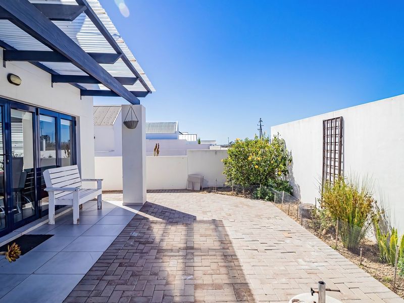 A well-maintained paved patio area featuring a timber pergola, sliding glass doors, and a private enclosed garden space.