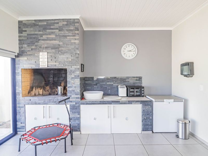 Covered patio area featuring a built-in braai with stone cladding, tiled flooring, and integrated cabinetry with a sink.