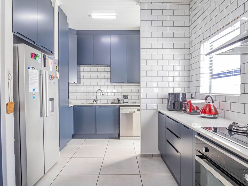Modern kitchen featuring dark blue cabinetry, white subway tile backsplash, stainless steel appliances, and tiled flooring.