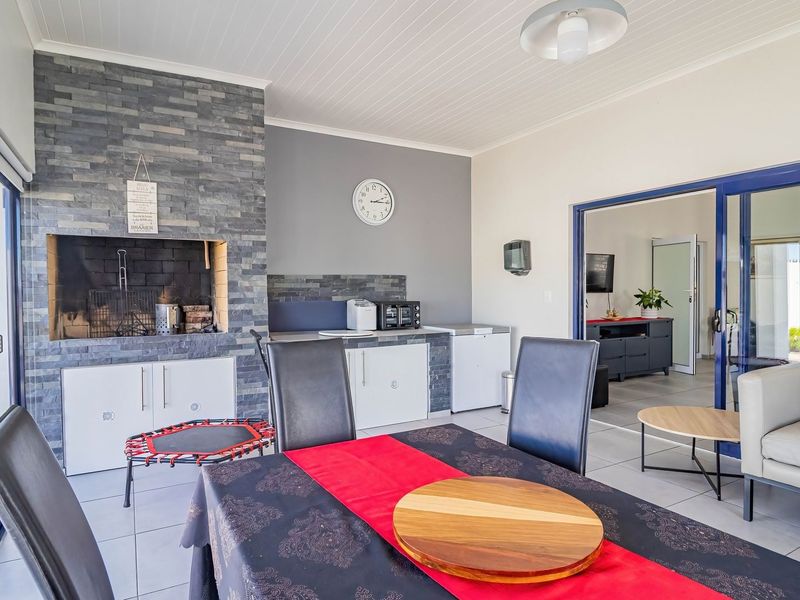 A spacious covered patio featuring a built-in braai with stone cladding, tiled flooring, and large sliding glass doors leading to the interior living area.