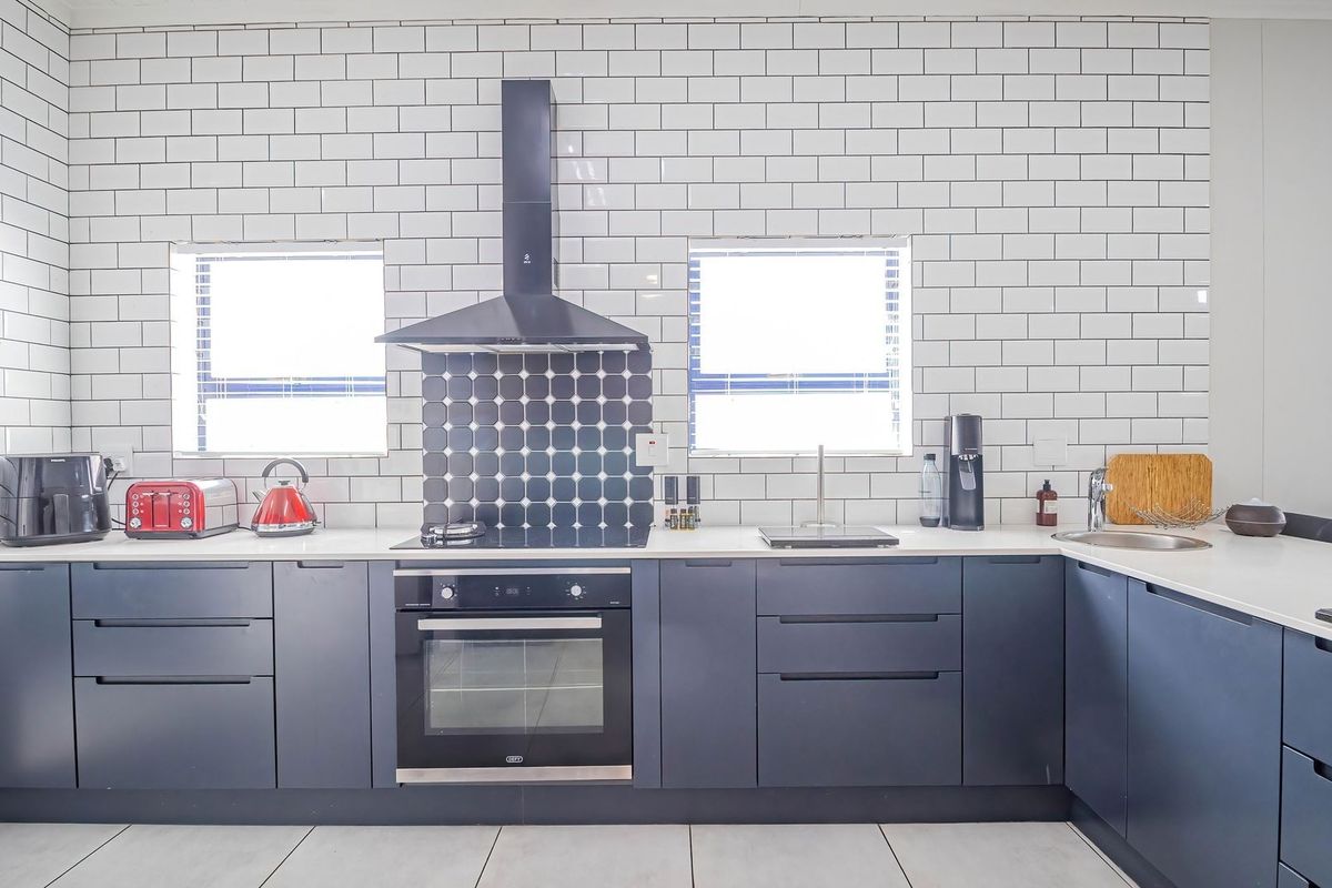 Modern kitchen featuring dark cabinetry, white subway tile backsplash, integrated oven, extractor fan, and clean quartz countertops with an undermount sink.