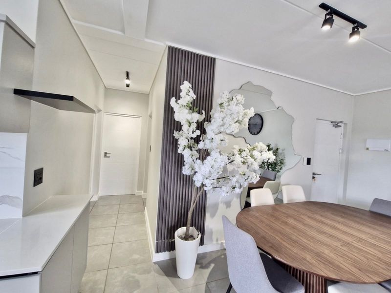 Modern open-plan living and dining area featuring contemporary track lighting, stylish slatted wood wall paneling, and sleek tiled flooring throughout.