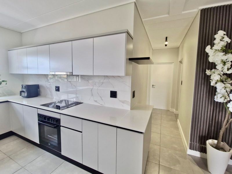 Modern kitchen featuring sleek white cabinetry, stone countertops, marble-look splashback, and integrated appliances, complemented by contemporary tiled flooring and decorative wall paneling.