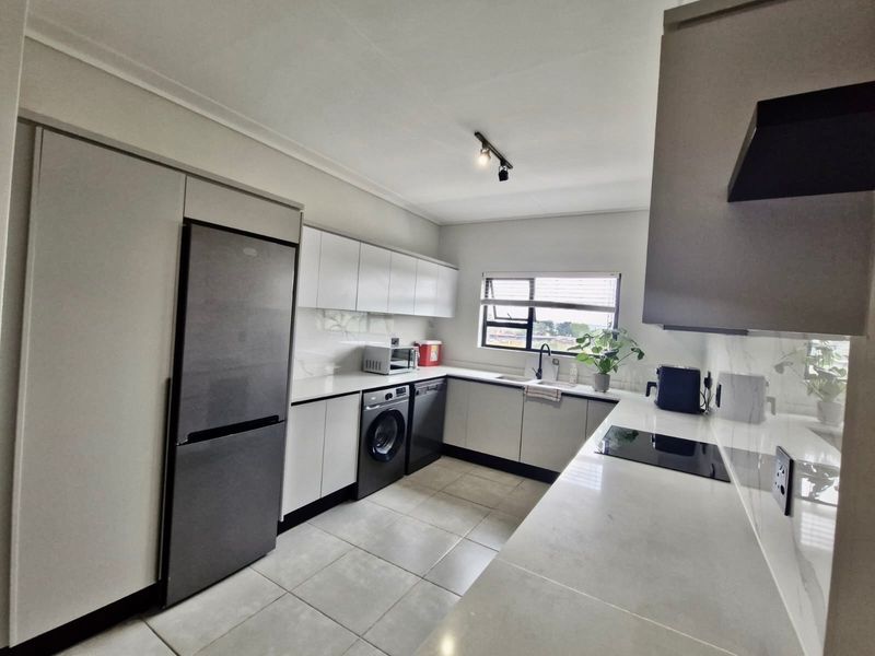 Modern kitchen featuring sleek white cabinetry, stone countertops, integrated hob, extractor fan, and tiled flooring in a clean, contemporary layout.