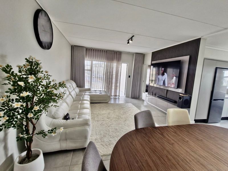 Modern open-plan living area featuring a stylish slatted wood media wall, tiled flooring, and seamless access to the balcony through large sliding glass doors.