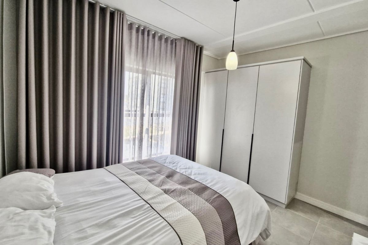 A well-maintained bedroom featuring neutral tiled flooring, a modern built-in wardrobe, and a contemporary pendant light fixture.