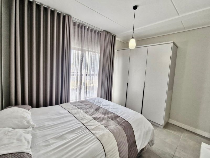 A well-maintained bedroom featuring neutral tiled flooring, a modern built-in wardrobe, and a contemporary pendant light fixture.