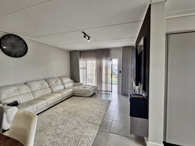 A modern living room featuring tiled flooring, contemporary track lighting, and a feature slatted wall panel, with direct access to an outdoor balcony.