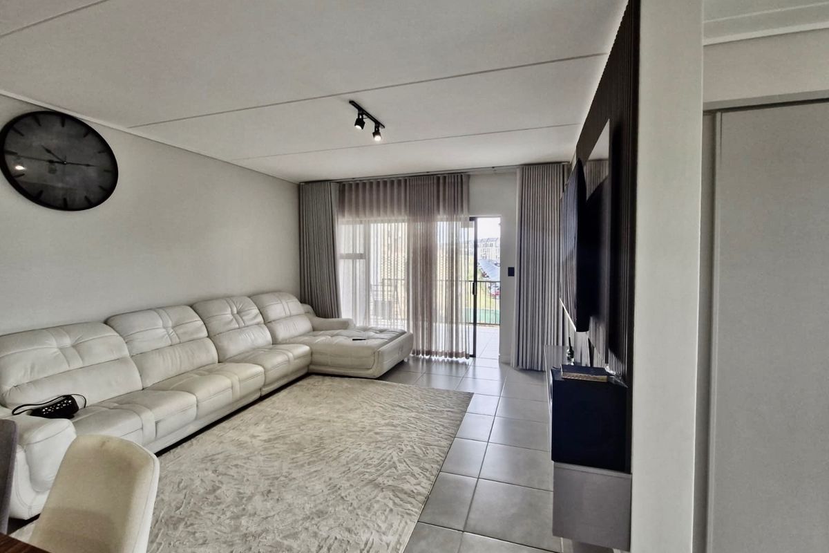 A modern living room featuring tiled flooring, contemporary track lighting, and a feature slatted wall panel, with direct access to an outdoor balcony.