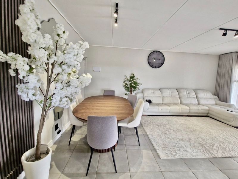 An open-plan living and dining area featuring neutral tiled flooring, modern track lighting, and decorative slatted wood wall paneling.