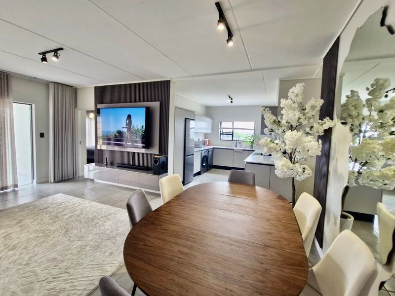 Modern open-plan living and kitchen area featuring contemporary track lighting, a stylish slatted feature wall, and sleek cabinetry with tiled flooring throughout.
