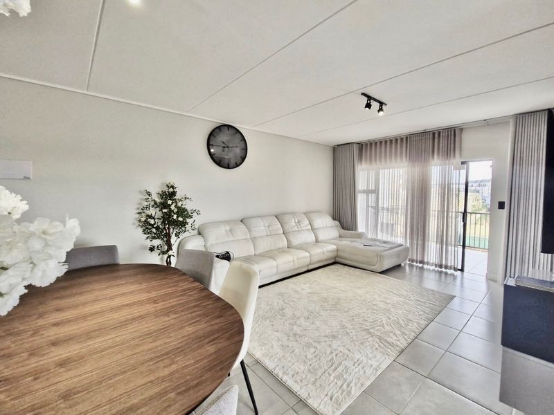 Bright open-plan living area featuring neutral tiled flooring, modern track lighting, and large sliding glass doors leading to an outdoor balcony.