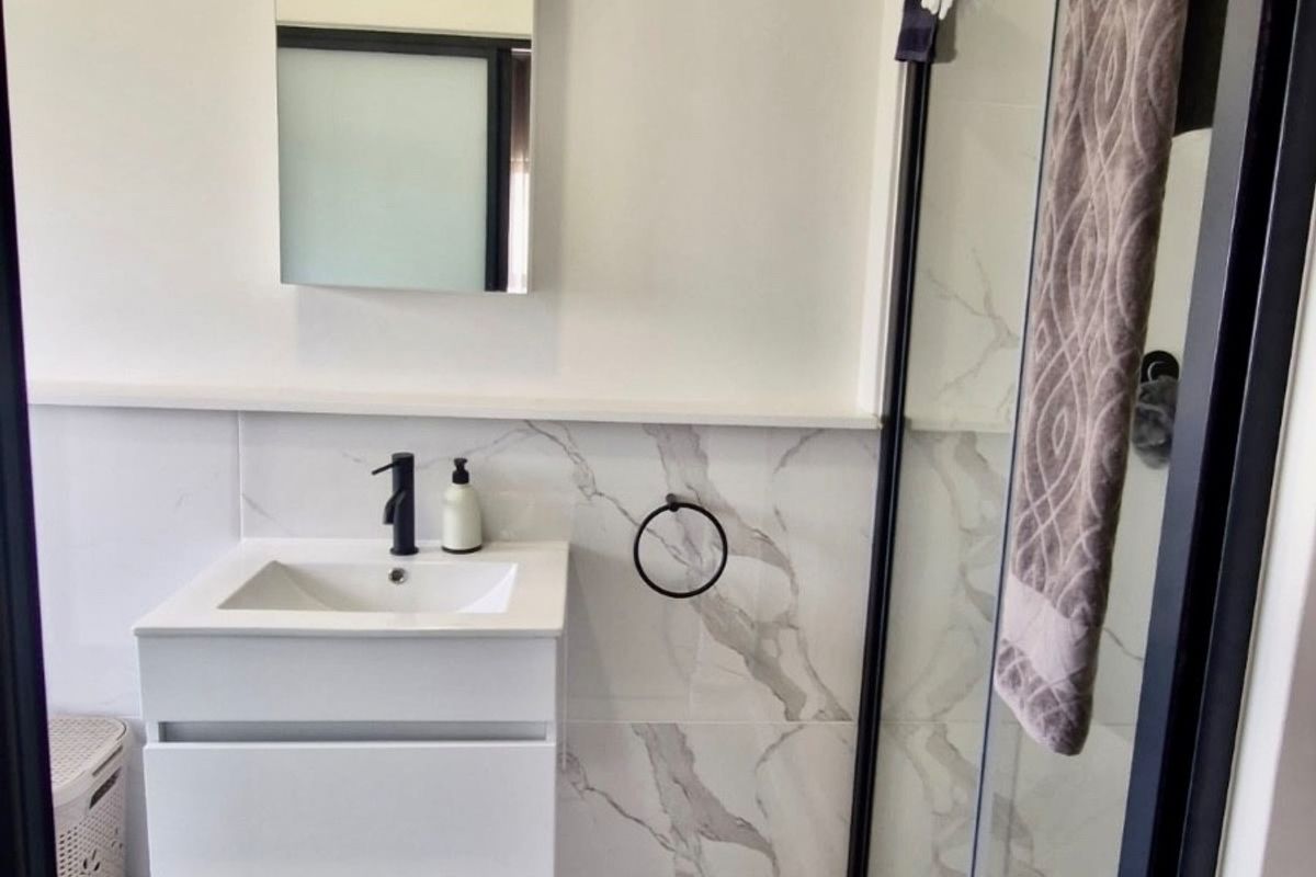 Modern bathroom featuring a wall-mounted vanity with a black mixer tap, marble-look wall tiling, and a glass shower enclosure with a black frame.