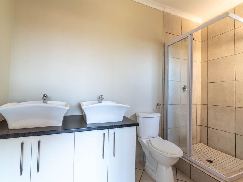 A clean, modern bathroom featuring a double vanity with white basins, a separate shower enclosure with tiled walls, and a standard toilet.