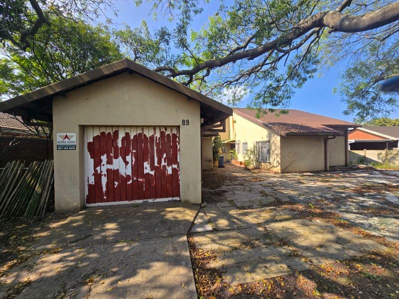 Front exterior view of the property featuring a single garage with a weathered door, paved driveway, and tiled roof structure.