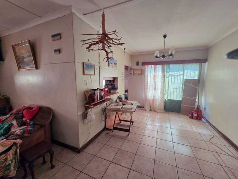 A living room featuring ceramic floor tiles, a sliding glass door with security gate, and a ceiling cornice, requiring cosmetic updates to improve condition.