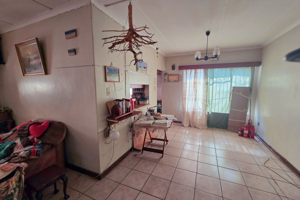 A living room featuring ceramic floor tiles, a sliding glass door with security gate, and a ceiling cornice, requiring cosmetic updates to improve condition.