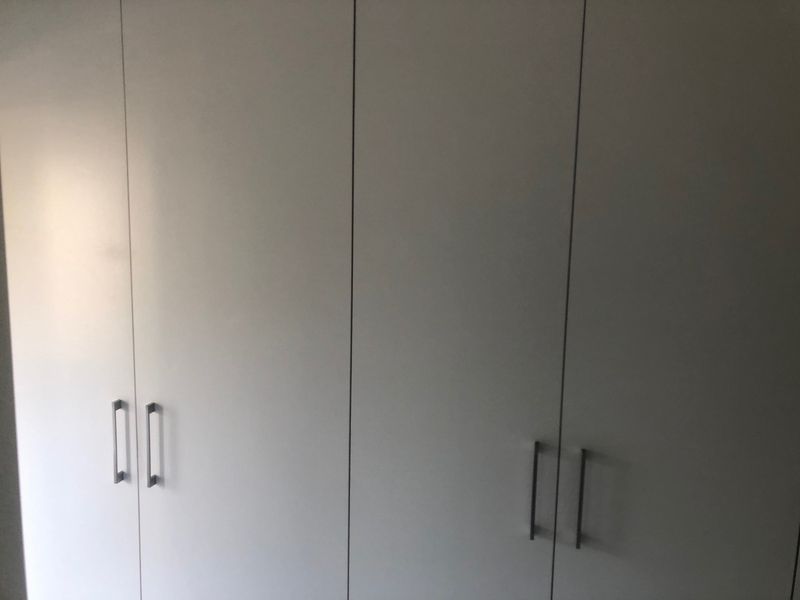 A close-up view of modern, white built-in cupboards with metallic handles, providing ample storage space within the bedroom.