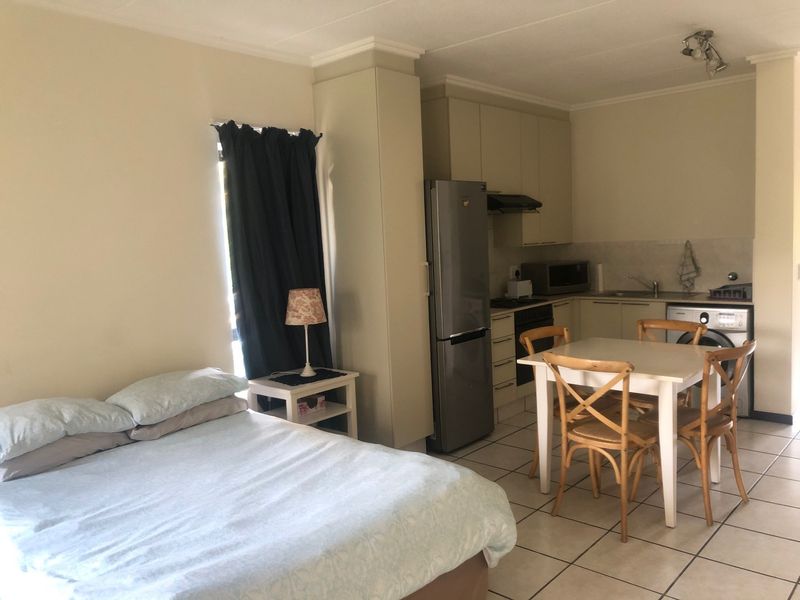 An open-plan studio apartment featuring a compact kitchen with built-in cabinetry, tiled flooring, and a combined living and sleeping area.