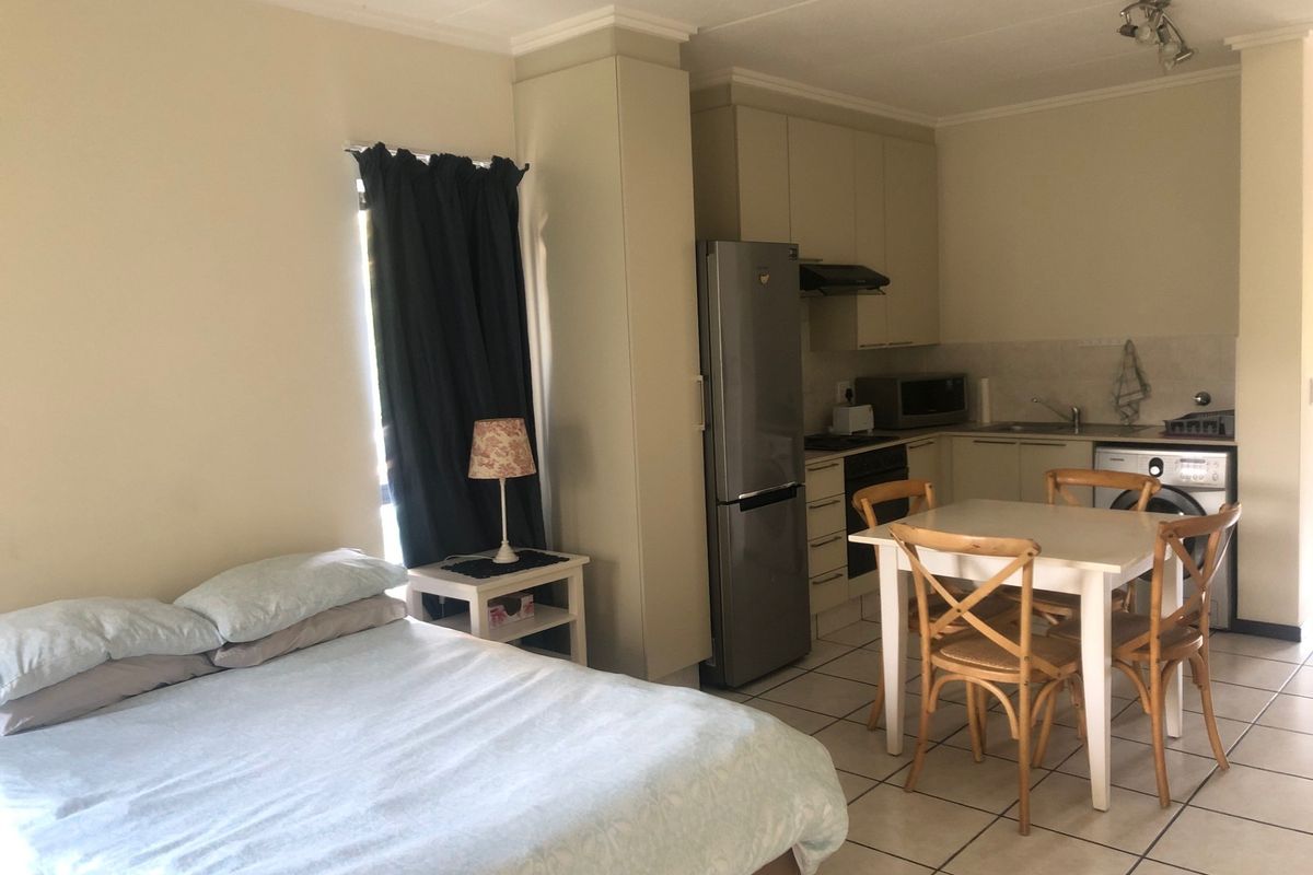 An open-plan studio apartment featuring a compact kitchen with built-in cabinetry, tiled flooring, and a combined living and sleeping area.