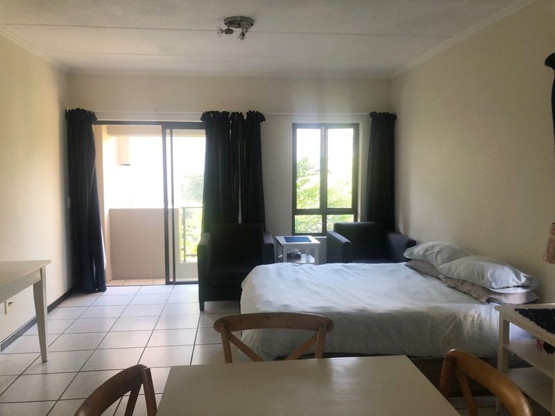 A bedroom featuring tiled flooring, a sliding glass door leading to a balcony, and a window providing natural light.