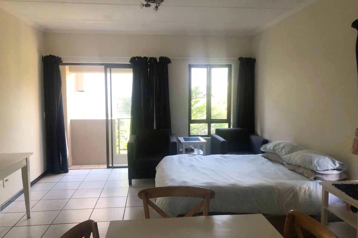 A bedroom featuring tiled flooring, a sliding glass door leading to a balcony, and a window providing natural light.
