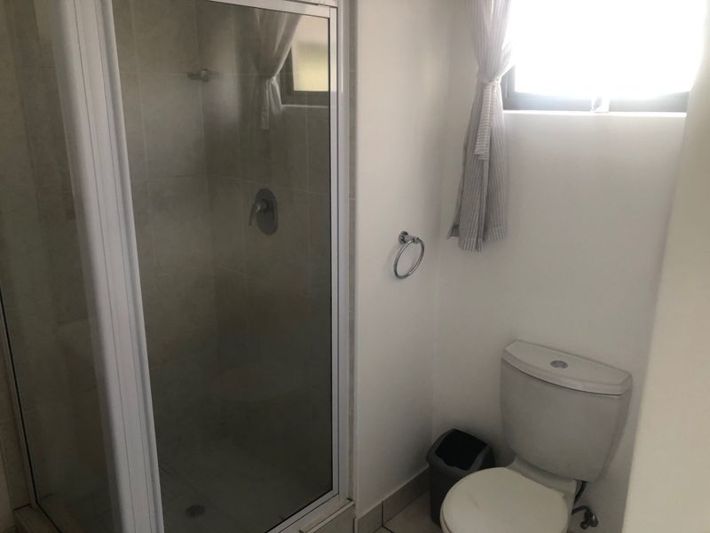 A functional bathroom featuring a glass-enclosed shower and a standard toilet, finished with neutral wall tiles and flooring.
