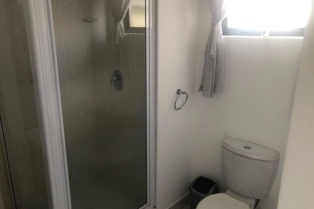 A functional bathroom featuring a glass-enclosed shower and a standard toilet, finished with neutral wall tiles and flooring.