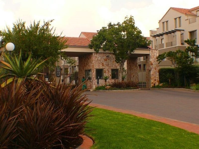 The entrance to the apartment complex features a secure gatehouse with stone cladding, paved driveway, and well-maintained landscaped gardens.