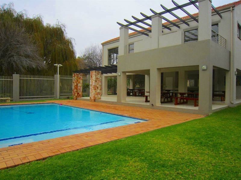 A well-maintained outdoor area featuring a swimming pool, brick-paved surround, and a spacious covered patio with a pergola and stone-clad pillars.