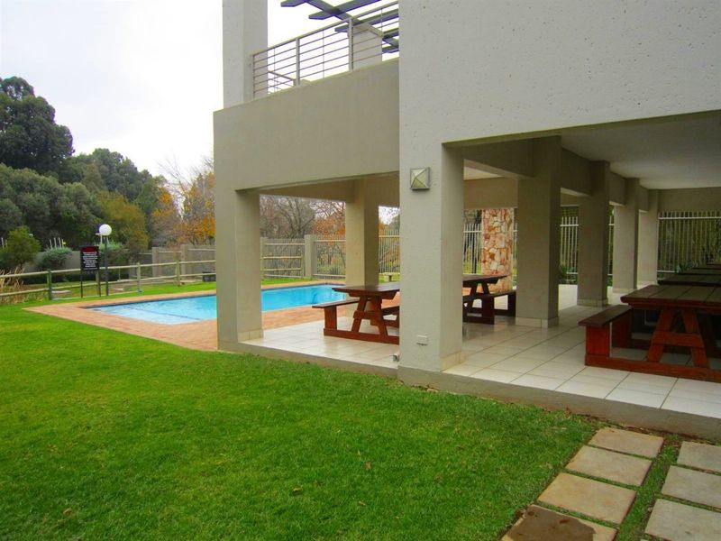 A covered outdoor patio area overlooking a swimming pool, featuring tiled flooring, stone accents, and direct access to the garden.