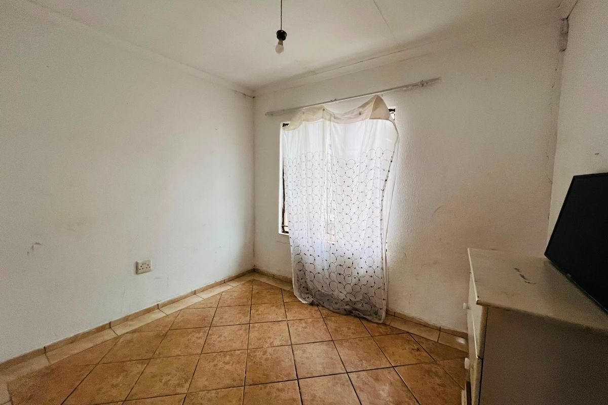 A simple, empty bedroom featuring tiled flooring and a window with a curtain rod, requiring cosmetic updates to the wall finishes.