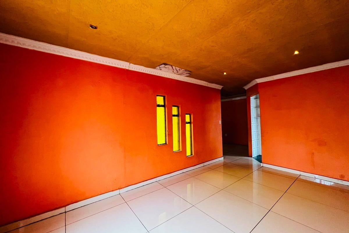 An empty living area featuring bright orange walls, tiled flooring, decorative ceiling cornices, and unique vertical feature windows.