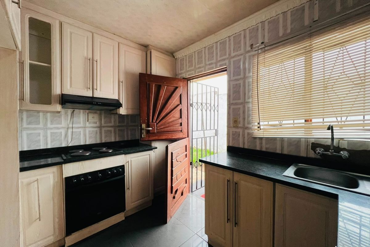 A functional kitchen featuring built-in cabinetry, black granite countertops, an integrated stove with extractor fan, and direct access to the exterior.