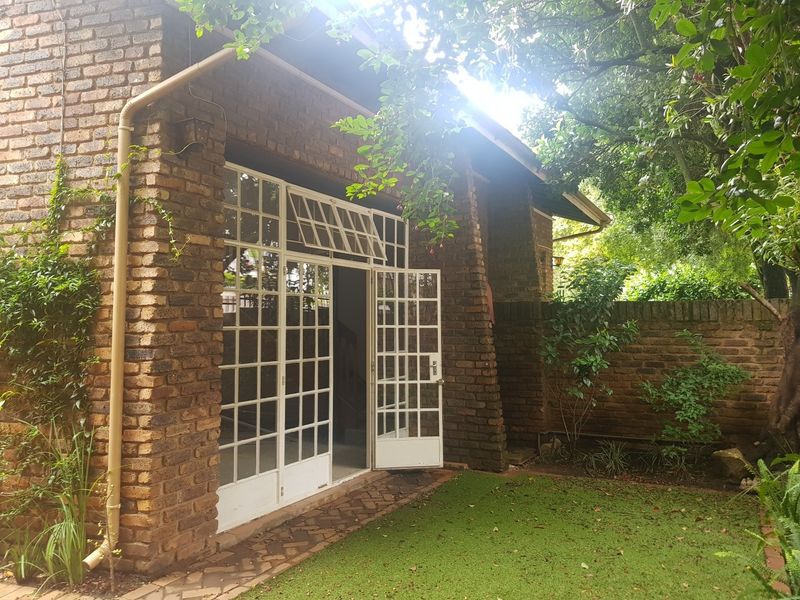 A rear view of the house featuring a face brick facade, white-framed french doors, and a small garden area with a brick boundary wall.