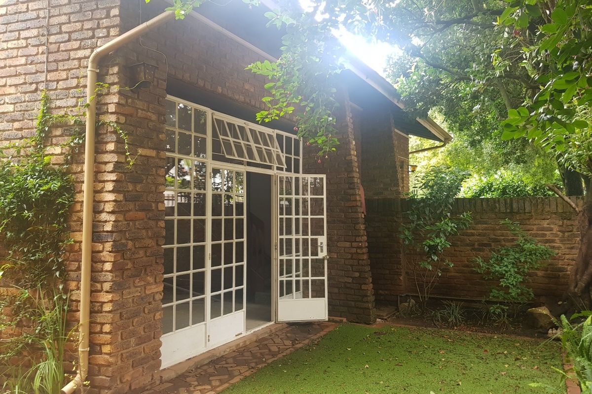 A rear view of the house featuring a face brick facade, white-framed french doors, and a small garden area with a brick boundary wall.