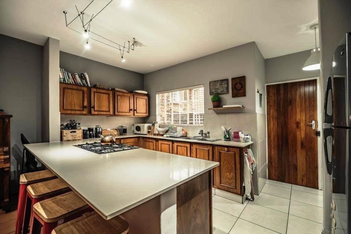 A well-appointed kitchen featuring timber cabinetry, stone countertops, a central gas hob, and tiled flooring, complemented by modern track lighting.
