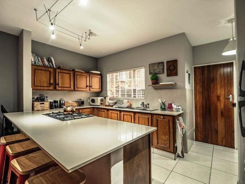 A well-appointed kitchen featuring timber cabinetry, stone countertops, a central gas hob, and tiled flooring, complemented by modern track lighting.