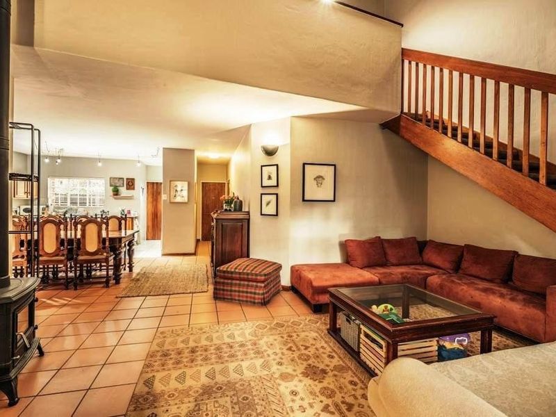 Spacious open-plan living and dining area featuring a wood-burning stove, tiled flooring, and a prominent timber staircase with a wooden balustrade.