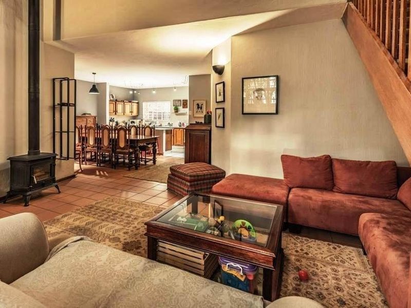 Open plan living area featuring a freestanding fireplace, tiled flooring, and a wooden staircase leading to the upper level, with an adjacent kitchen.