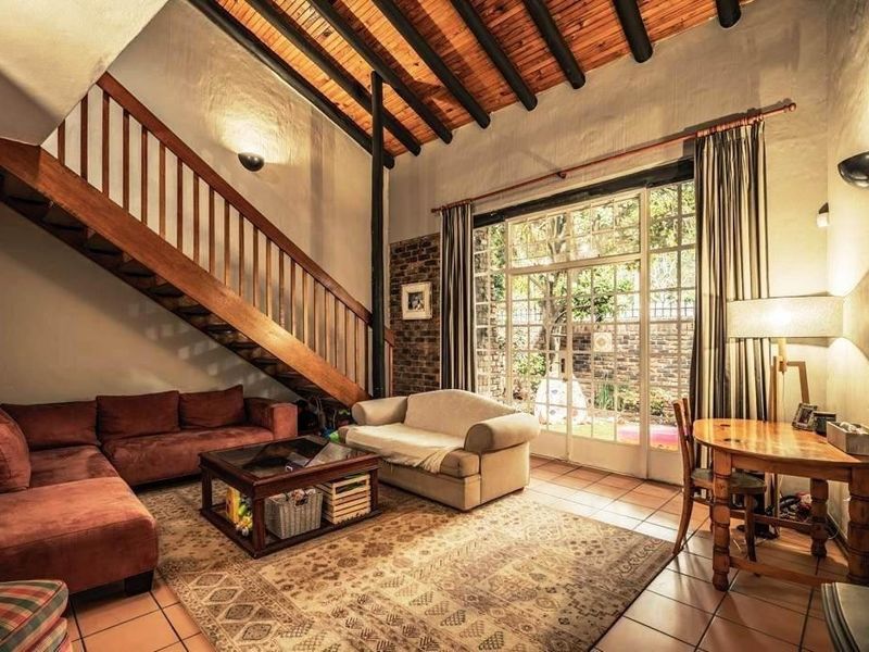 Spacious living room featuring a high exposed timber beam ceiling, a wooden staircase, and large glass doors opening to the garden.
