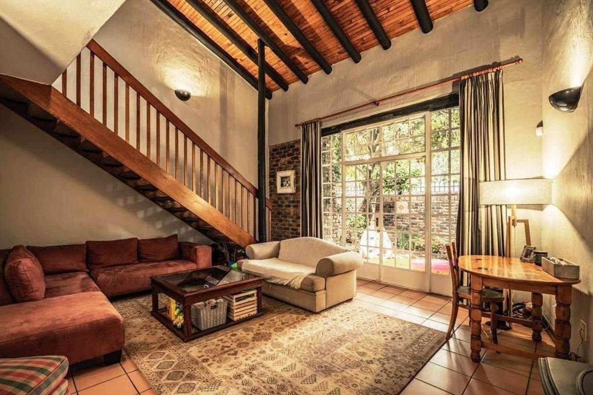 Spacious living room featuring a high exposed timber beam ceiling, a wooden staircase, and large glass doors opening to the garden.