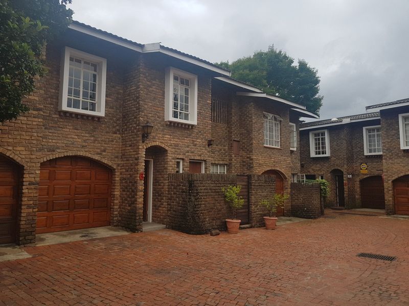 A charming multi-unit residential complex featuring classic face-brick architecture, arched garage doors, and a well-maintained paved courtyard entrance.