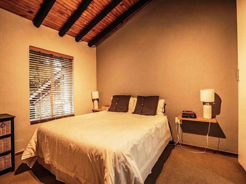 A cozy bedroom featuring a vaulted timber-beamed ceiling, carpeted flooring, and a built-in wardrobe, offering a warm and rustic atmosphere.