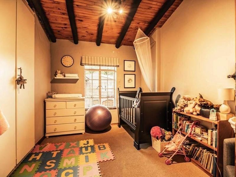 A cozy bedroom featuring exposed timber ceiling beams, built-in cupboards, and a window providing natural light.