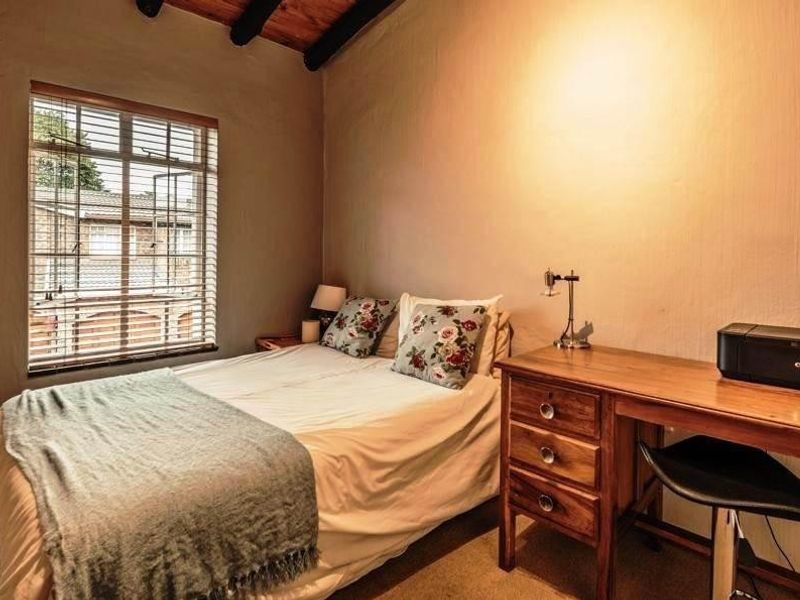 A cozy bedroom featuring exposed timber ceiling beams and a window with fitted venetian blinds.