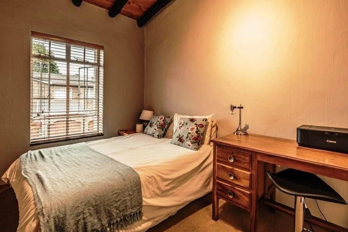 A cozy bedroom featuring exposed timber ceiling beams and a window with fitted venetian blinds.